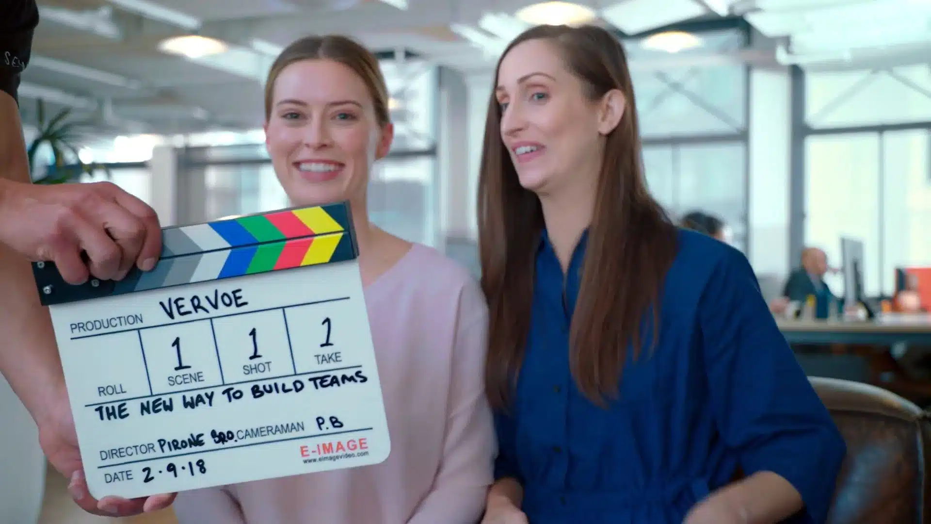 Two women in an office setting with a clapperboard 