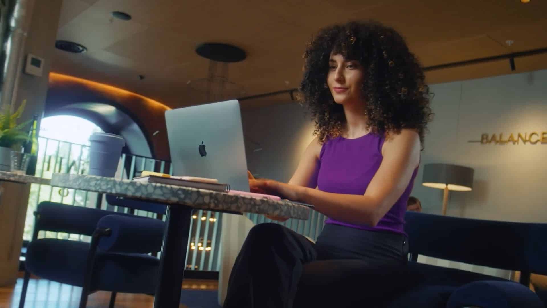 A woman with curly hair works on a laptop at a modern cafe table