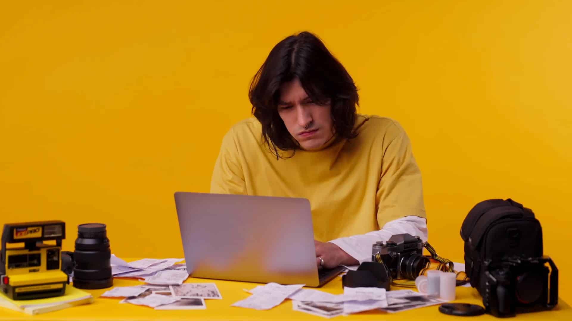 Man working on laptop with scattered photos and camera on the table