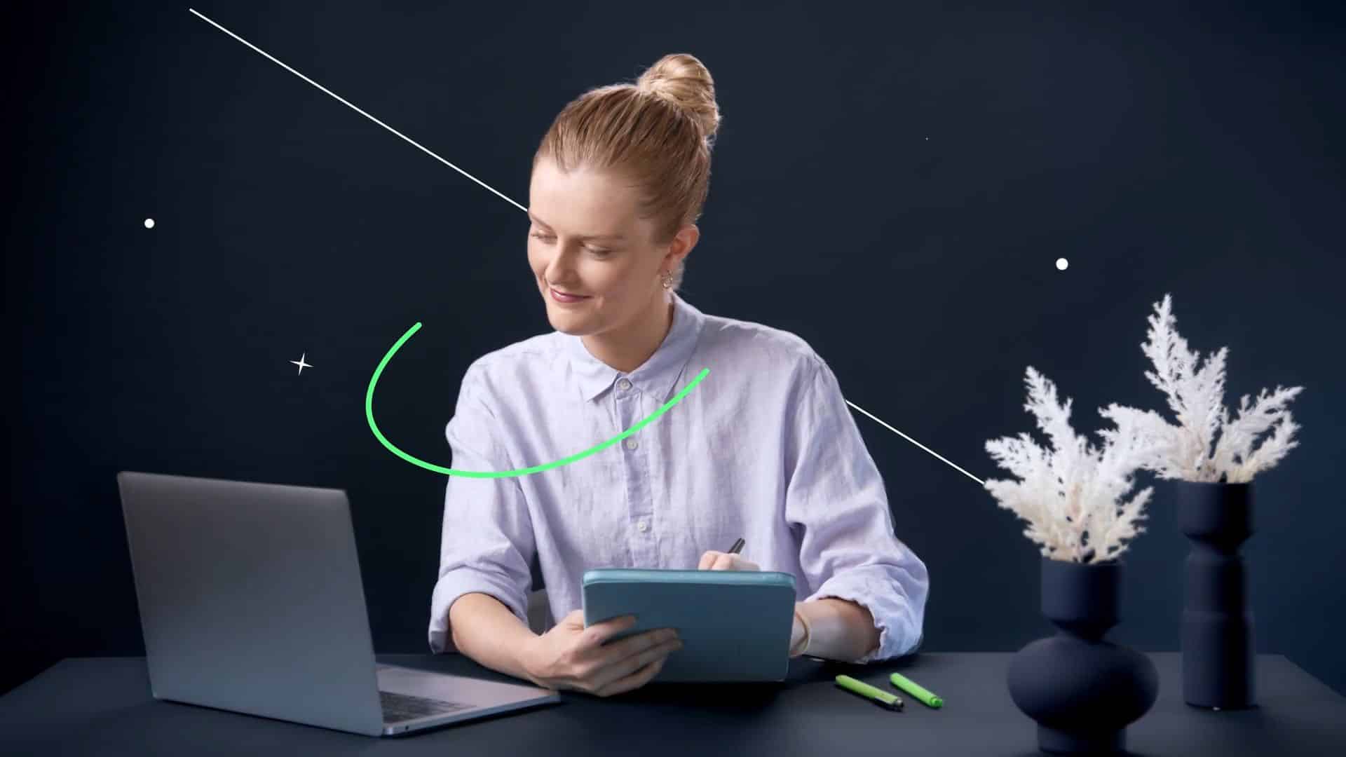 Woman using a tablet beside a laptop at a dark desk with simple graphic accents in the background